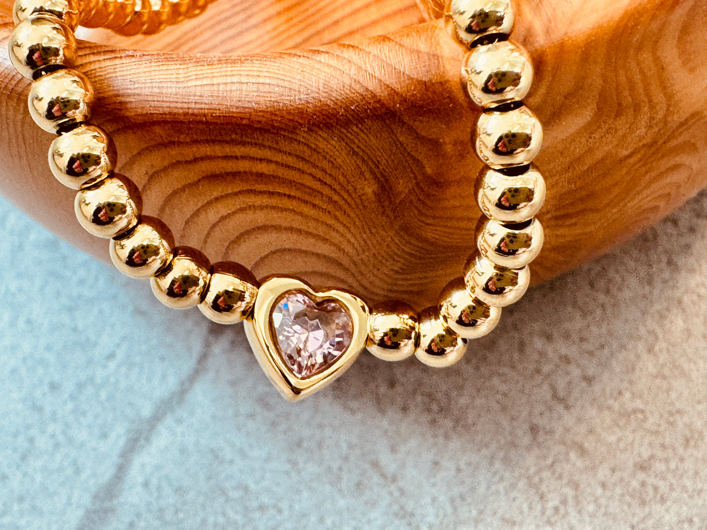 Gold beaded bracelet with a heart-shaped pink gemstone 